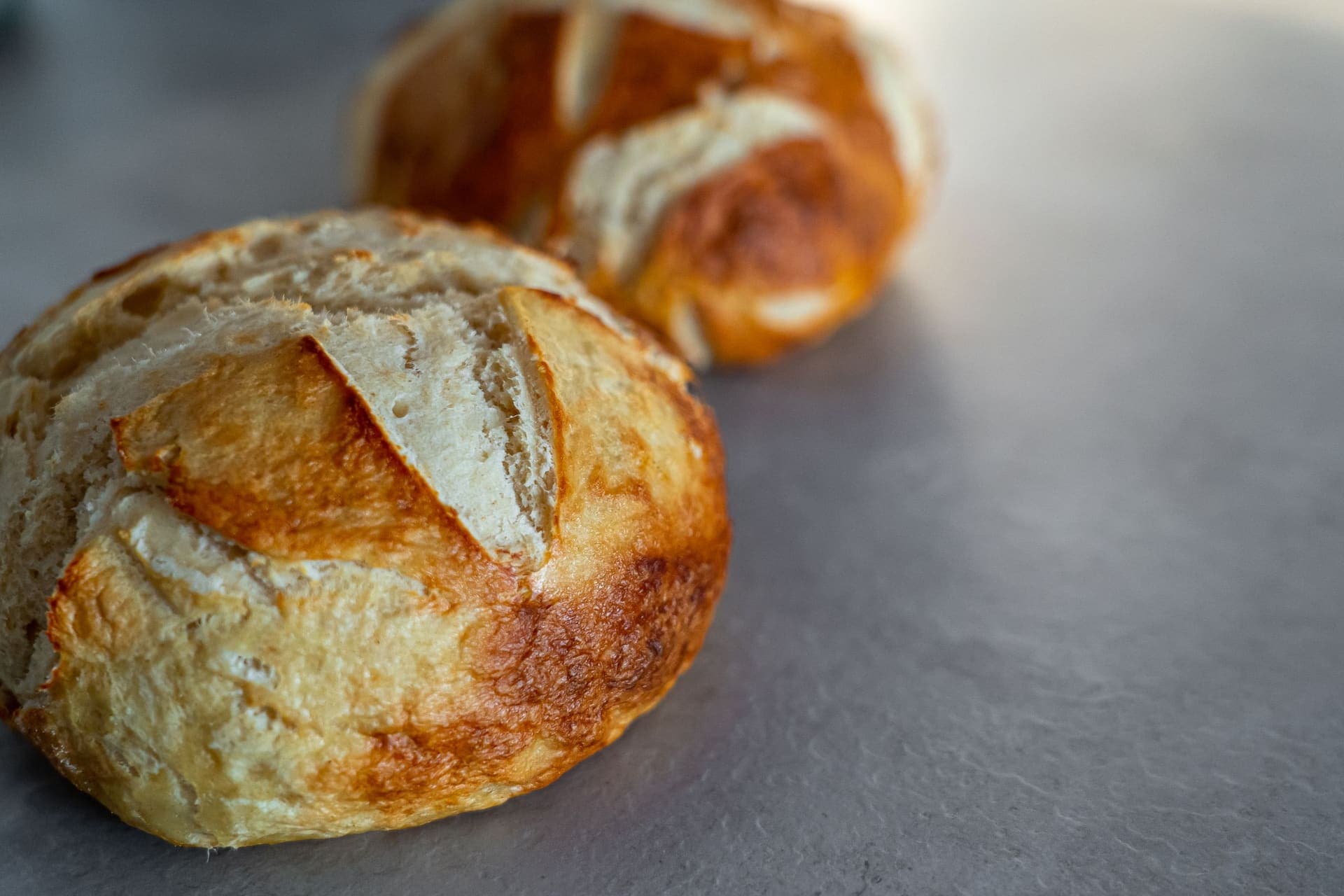 Two scored round bread rolls with golden crusts on a gray stone surface