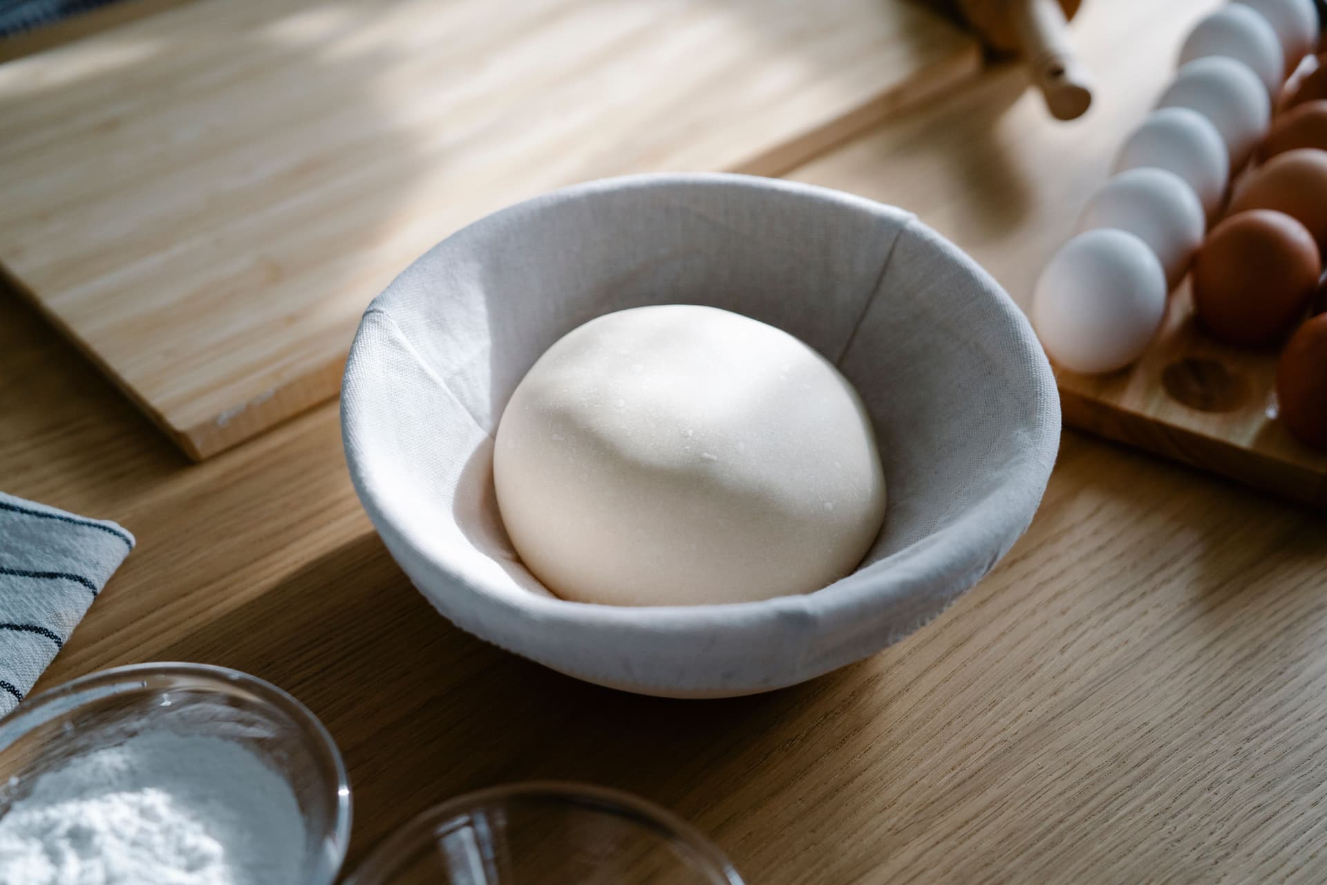 A mixing bowl lined with a cloth beside a shaped round of dough