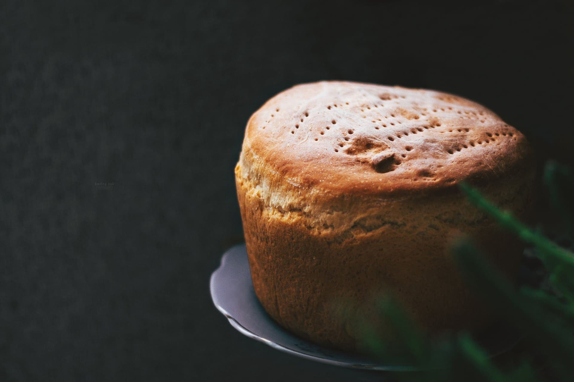 A scored loaf of fresh bread on a plate against a black background