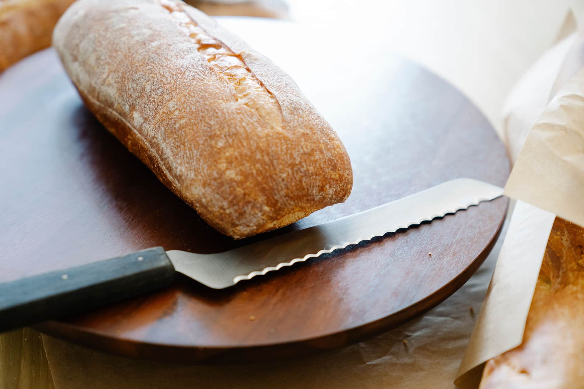 A freshly baked loaf on a wooden board beside a serrated bread knife