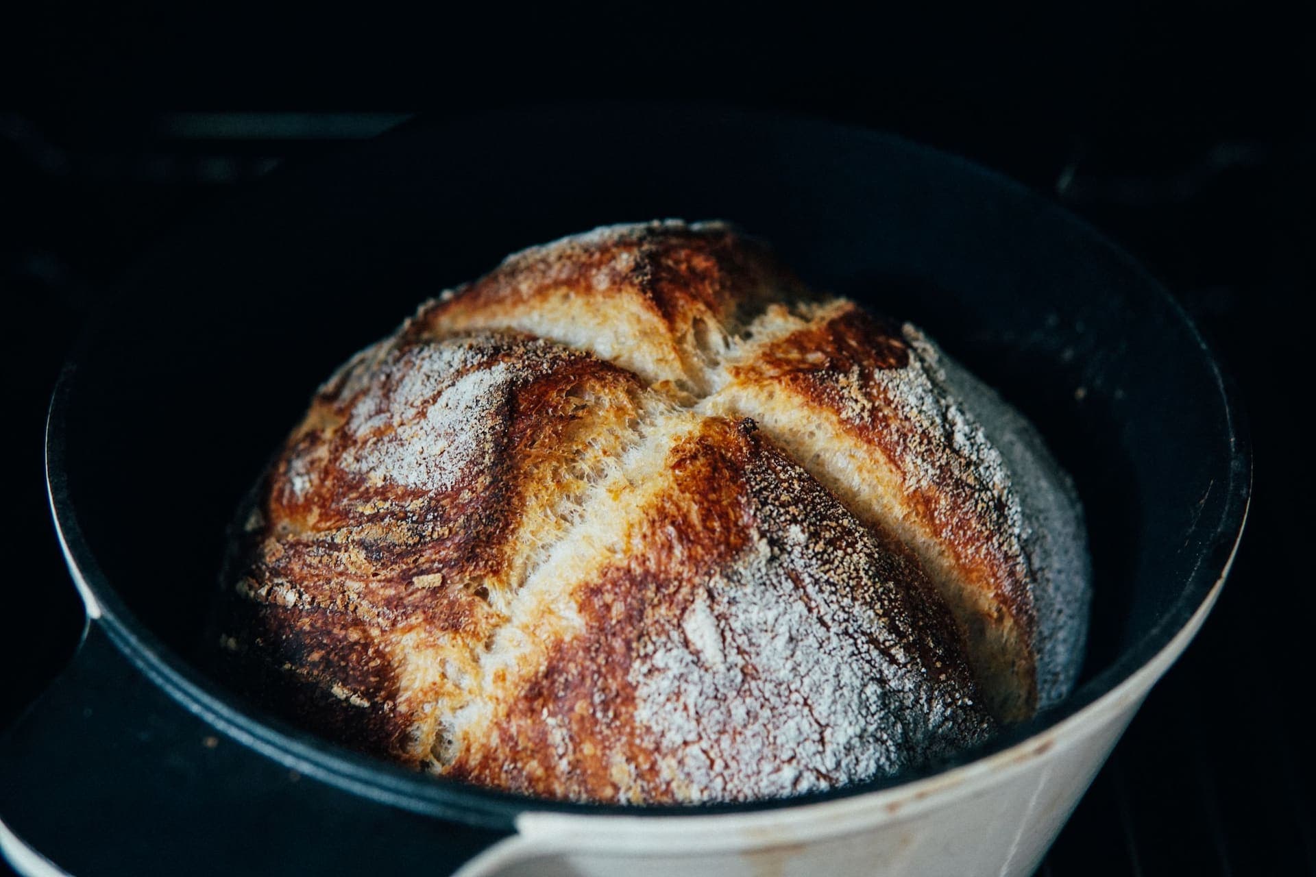 A scored round loaf baked in a dark cast iron pot