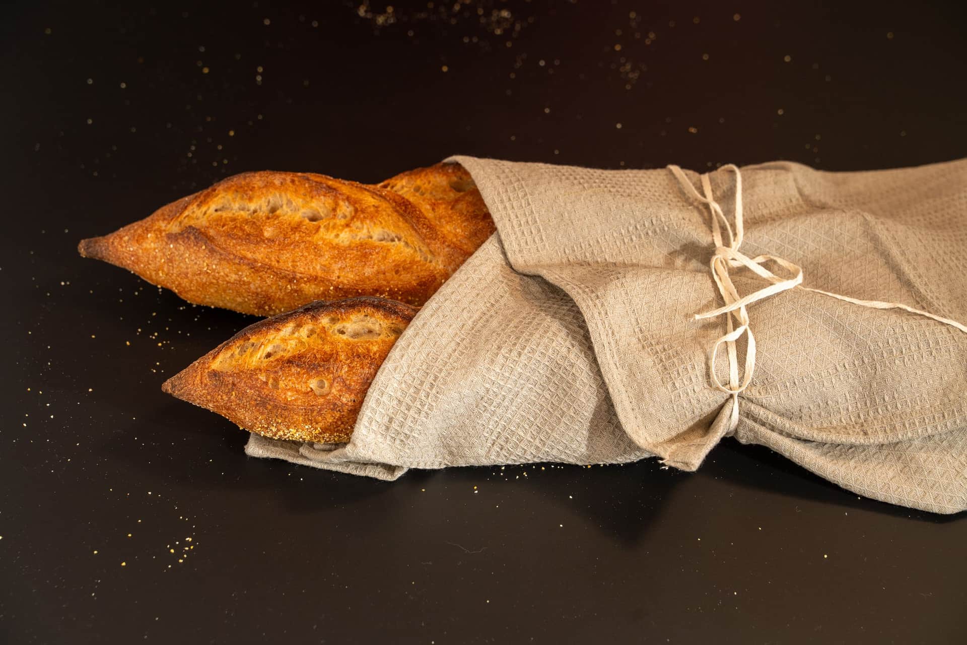 Two baguettes with golden scored crusts emerging from a folded linen cloth