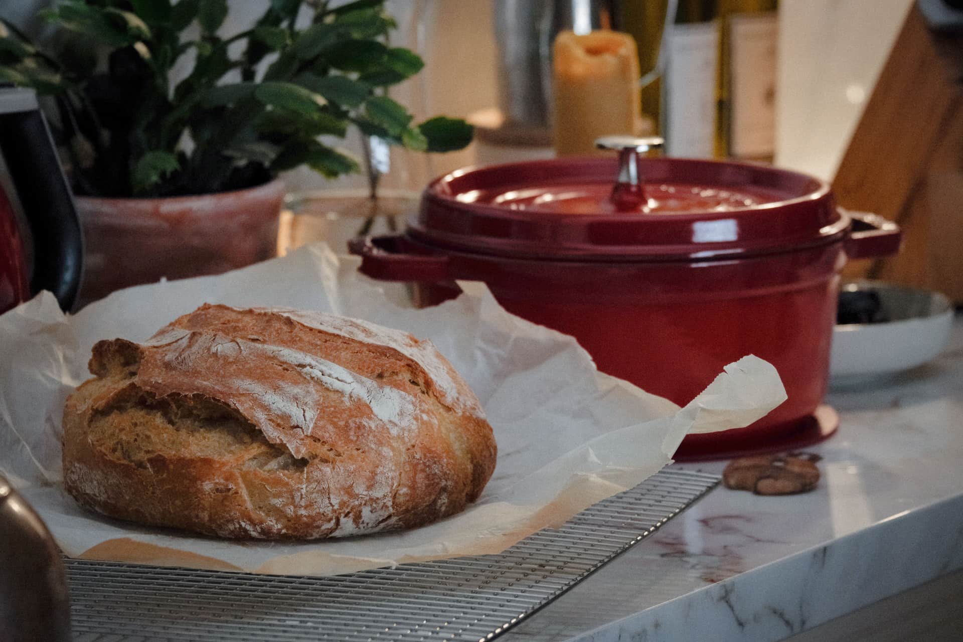 A rustic loaf of bread on a kitchen counter beside a red Dutch oven