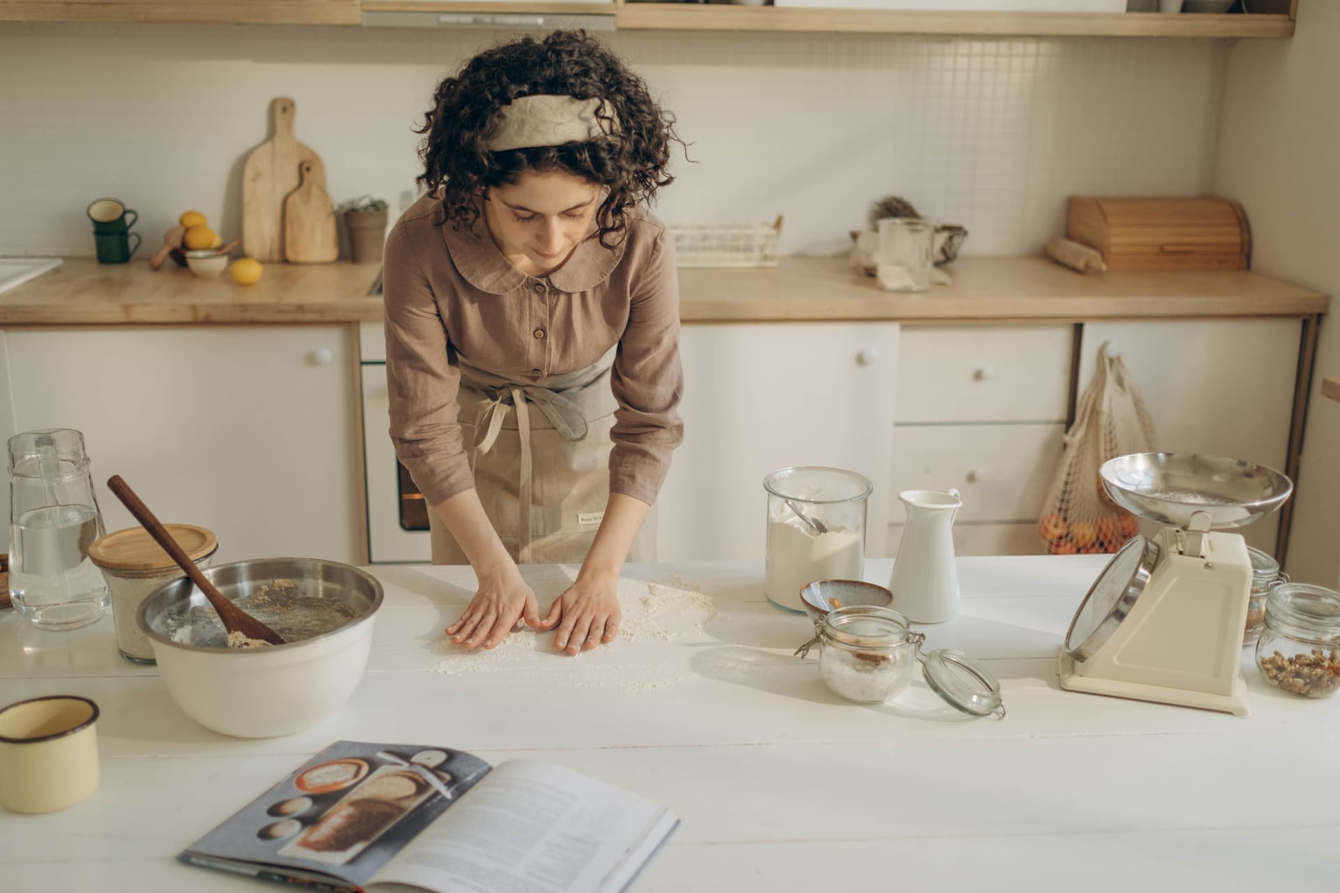 A digital kitchen scale, a bowl of flour and a glass jar arranged on a bare work surface
