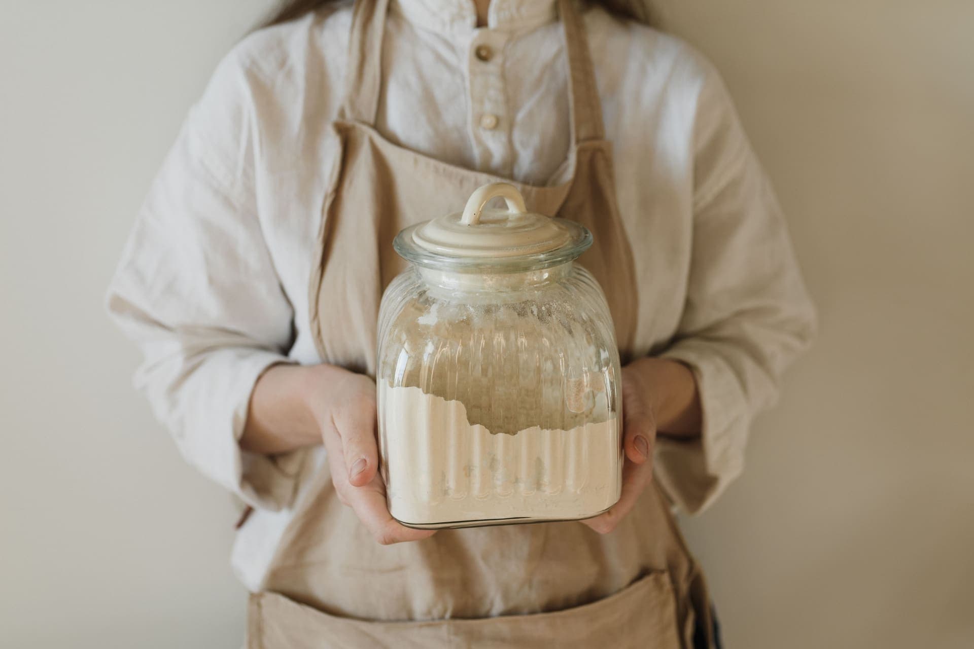 Hands in an apron holding a glass jar filled with pale flour