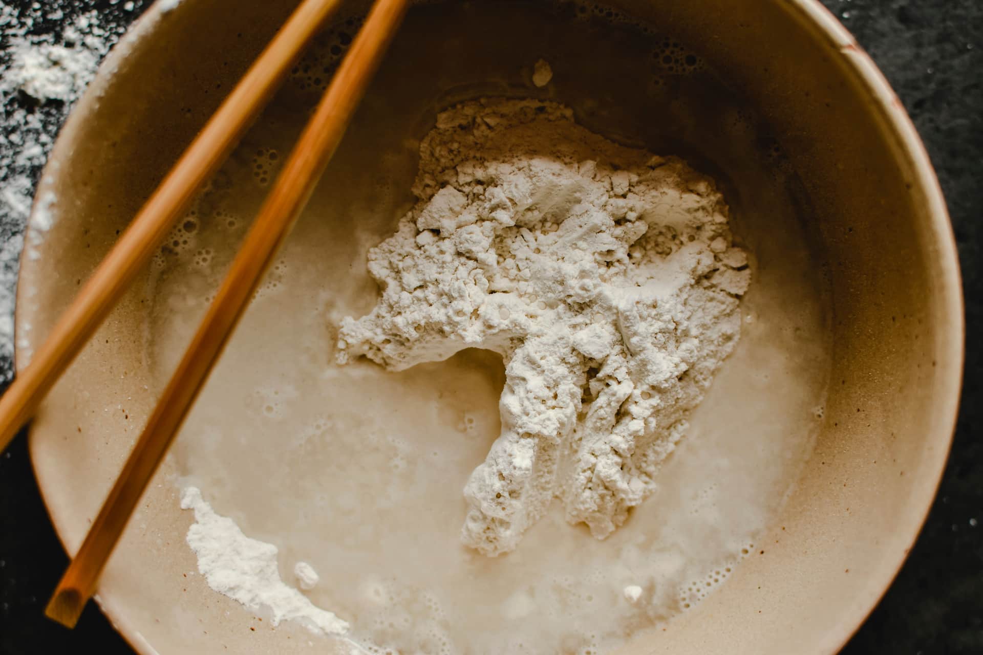 Flour and water being combined in a bowl with a wooden spoon
