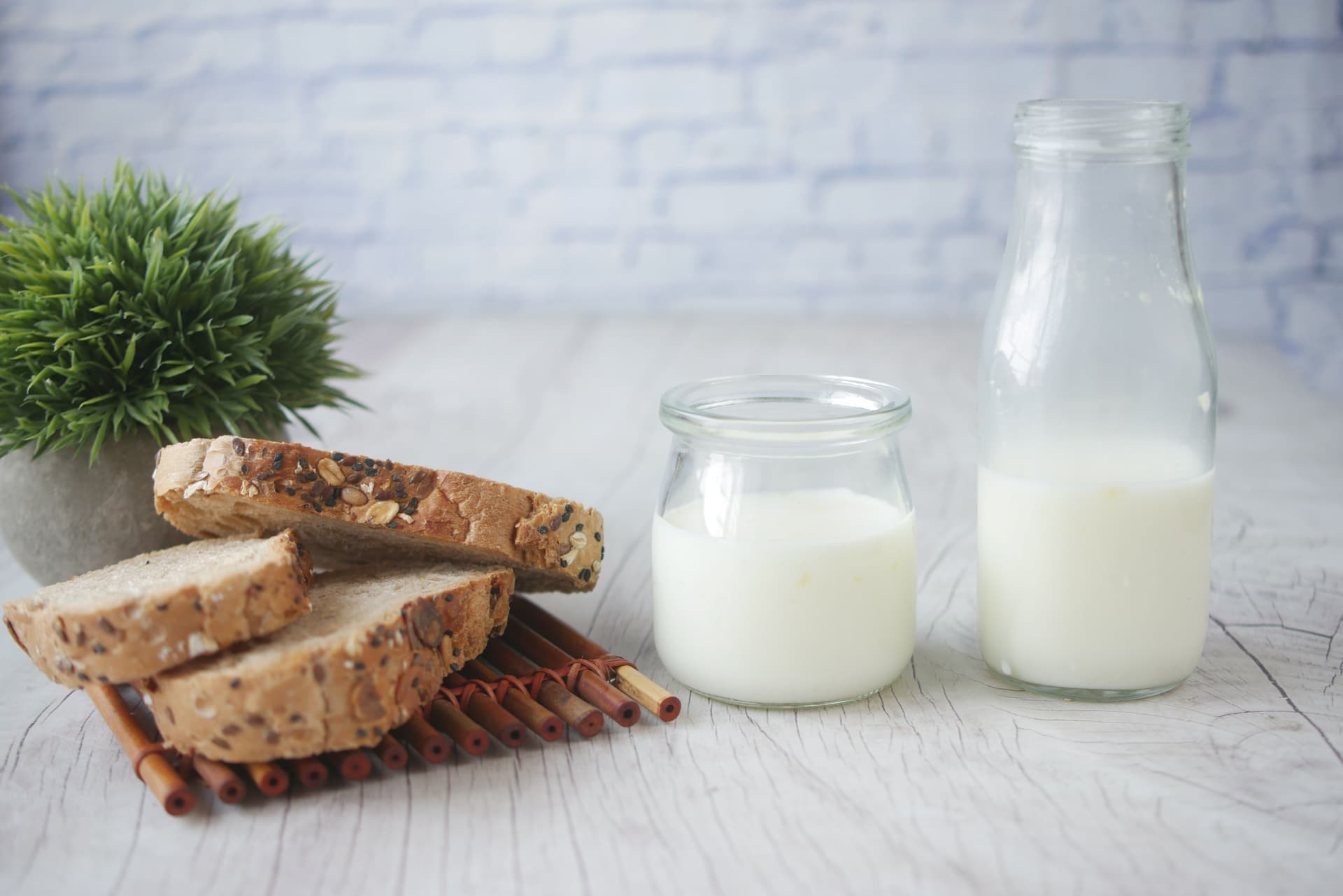 A glass of milk kefir beside a jar of grains on a kitchen surface
