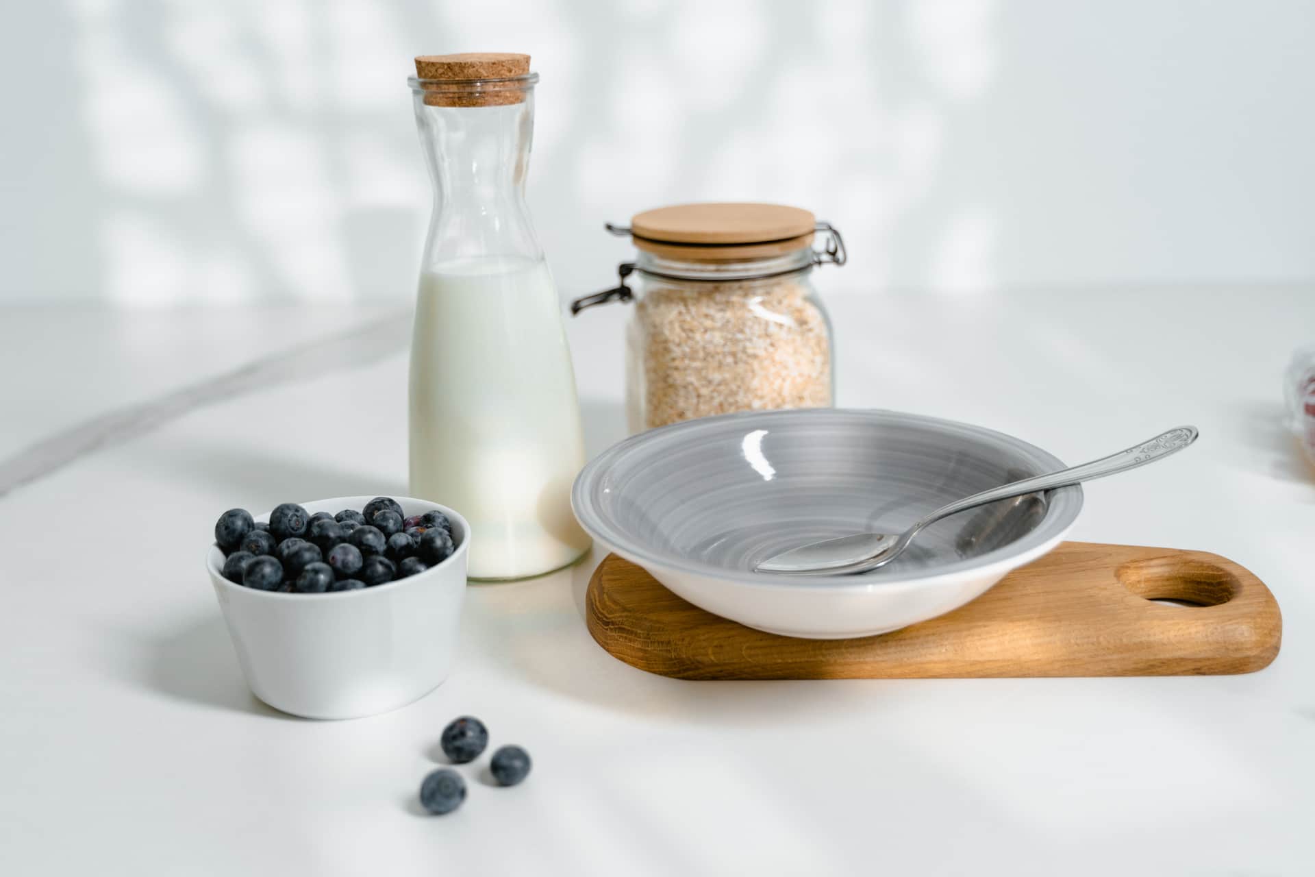 A glass of milk and a bowl of oats and blueberries on a bright kitchen counter