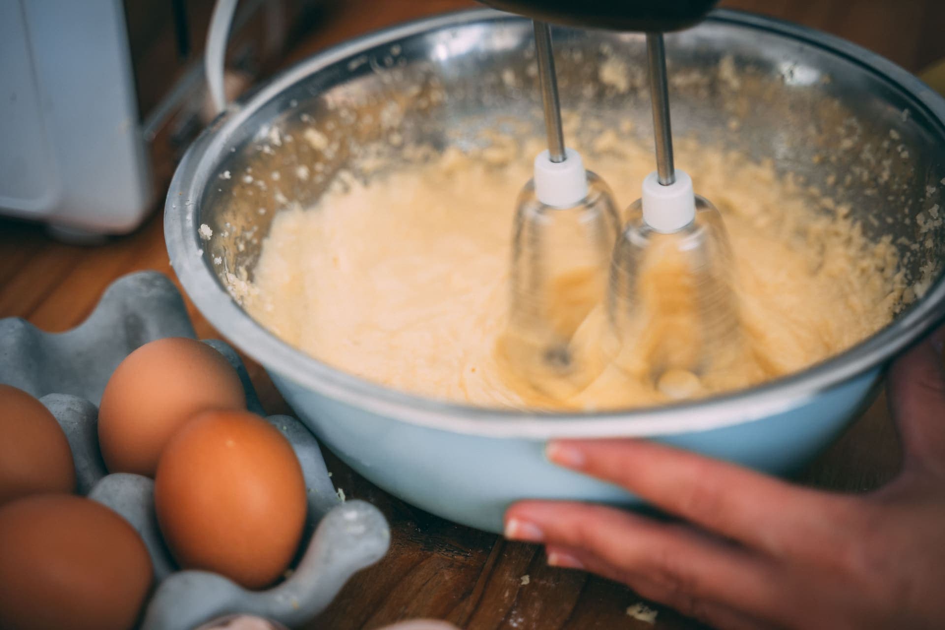 Batter being mixed in a bowl with eggs alongside on a wooden table
