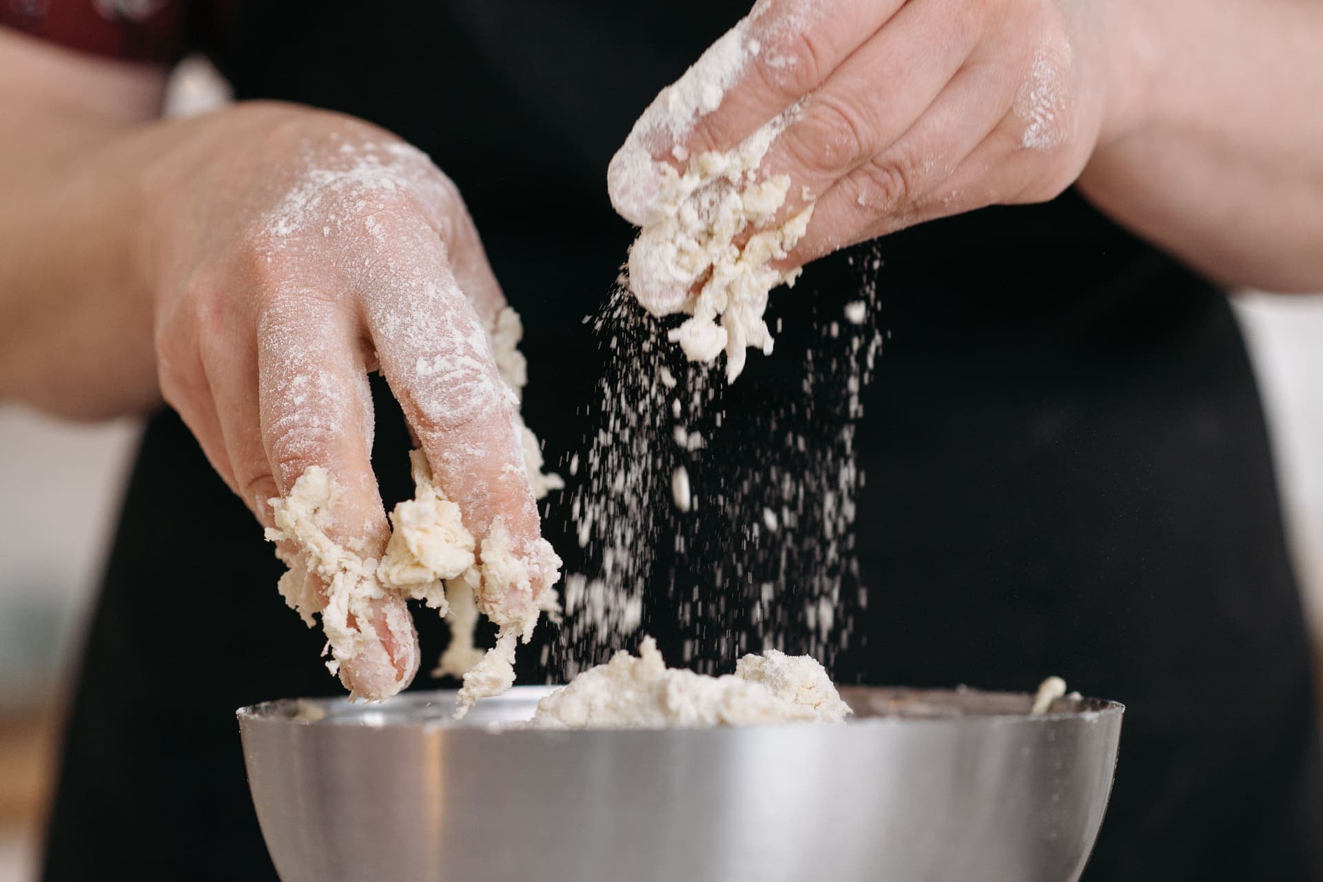 Hands working a shaggy dough in a stainless steel mixing bowl dusted with flour