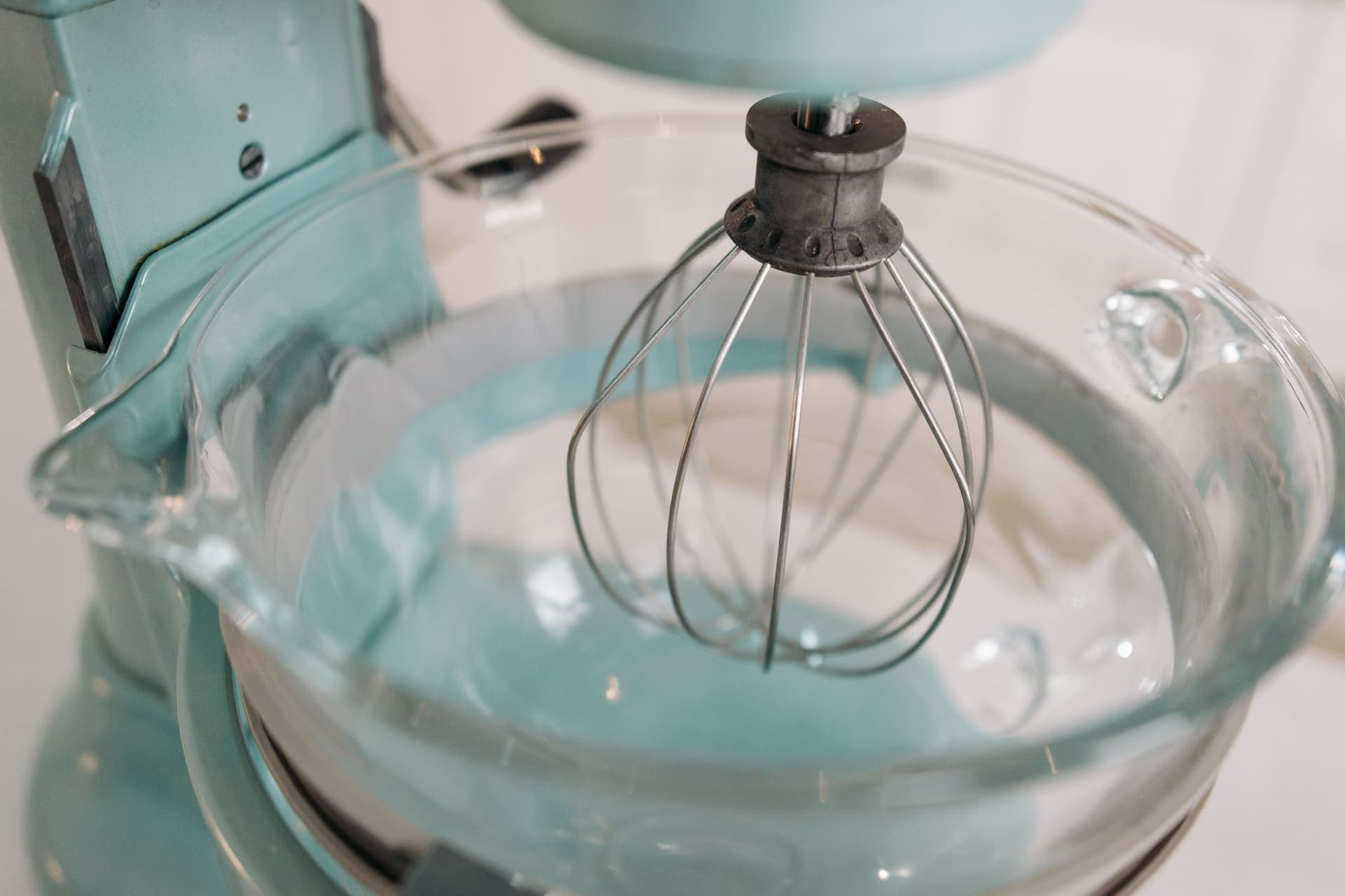 A stand mixer with a whisk attachment and a glass bowl, seen close up