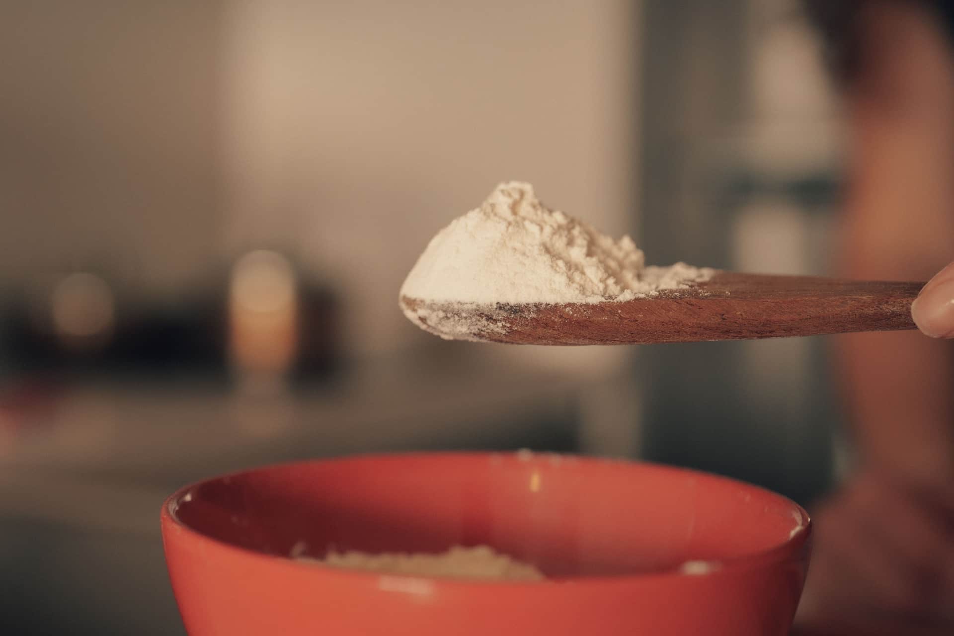 Flour on a wooden spoon held over a bowl in a kitchen