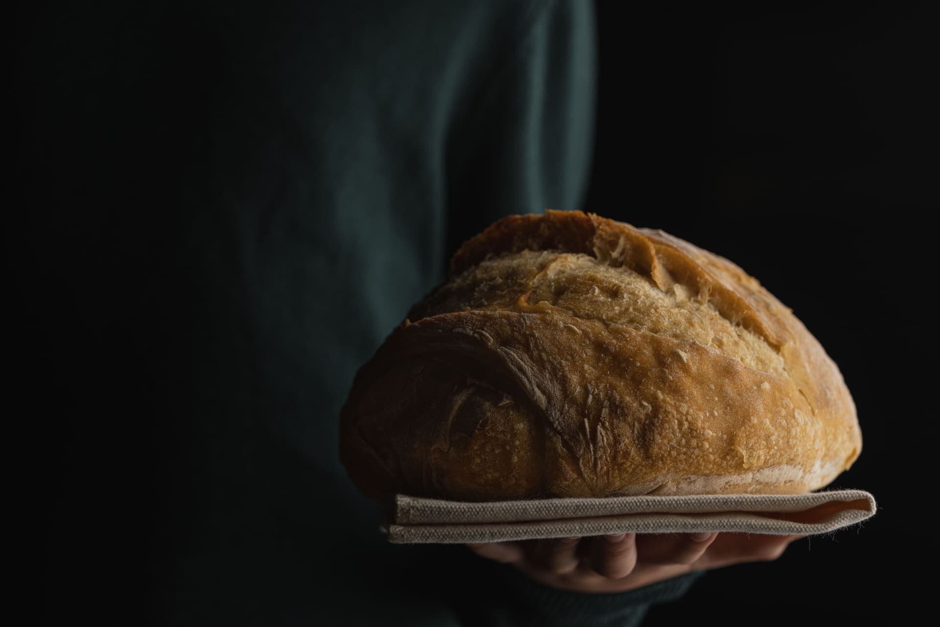 A dark close-up of a baked sourdough loaf held in two hands