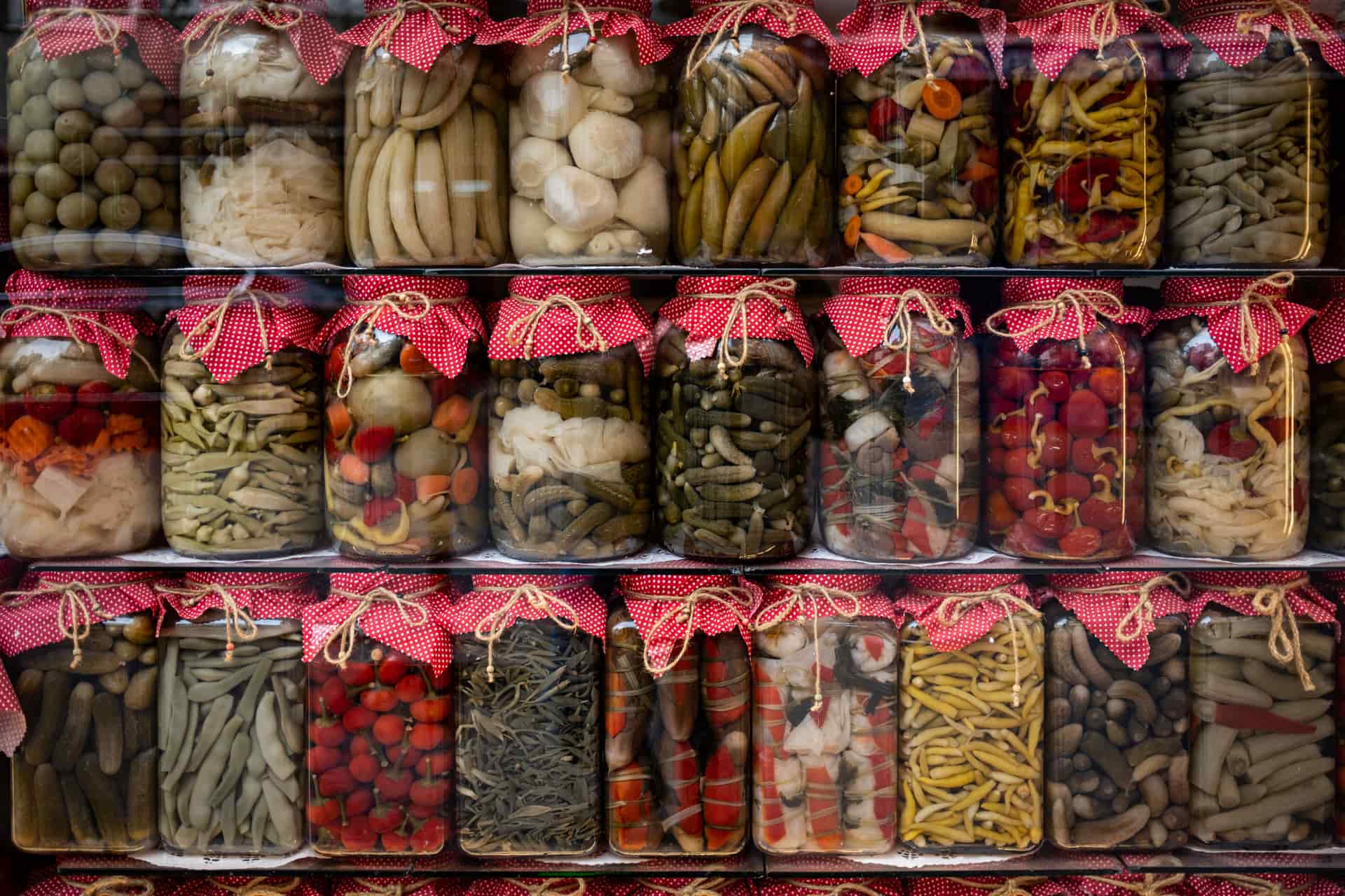 Several jars of fermented vegetables lined up on a wooden shelf