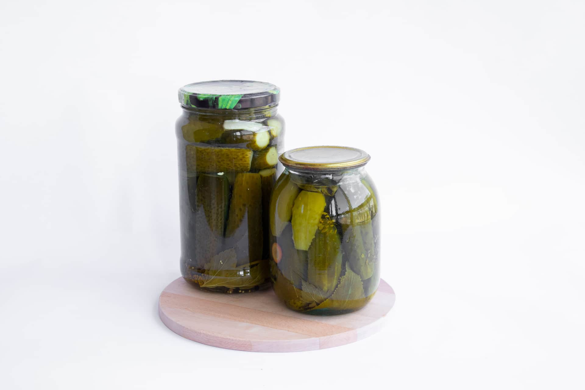 Two jars of pickled cucumbers in brine on a pale surface