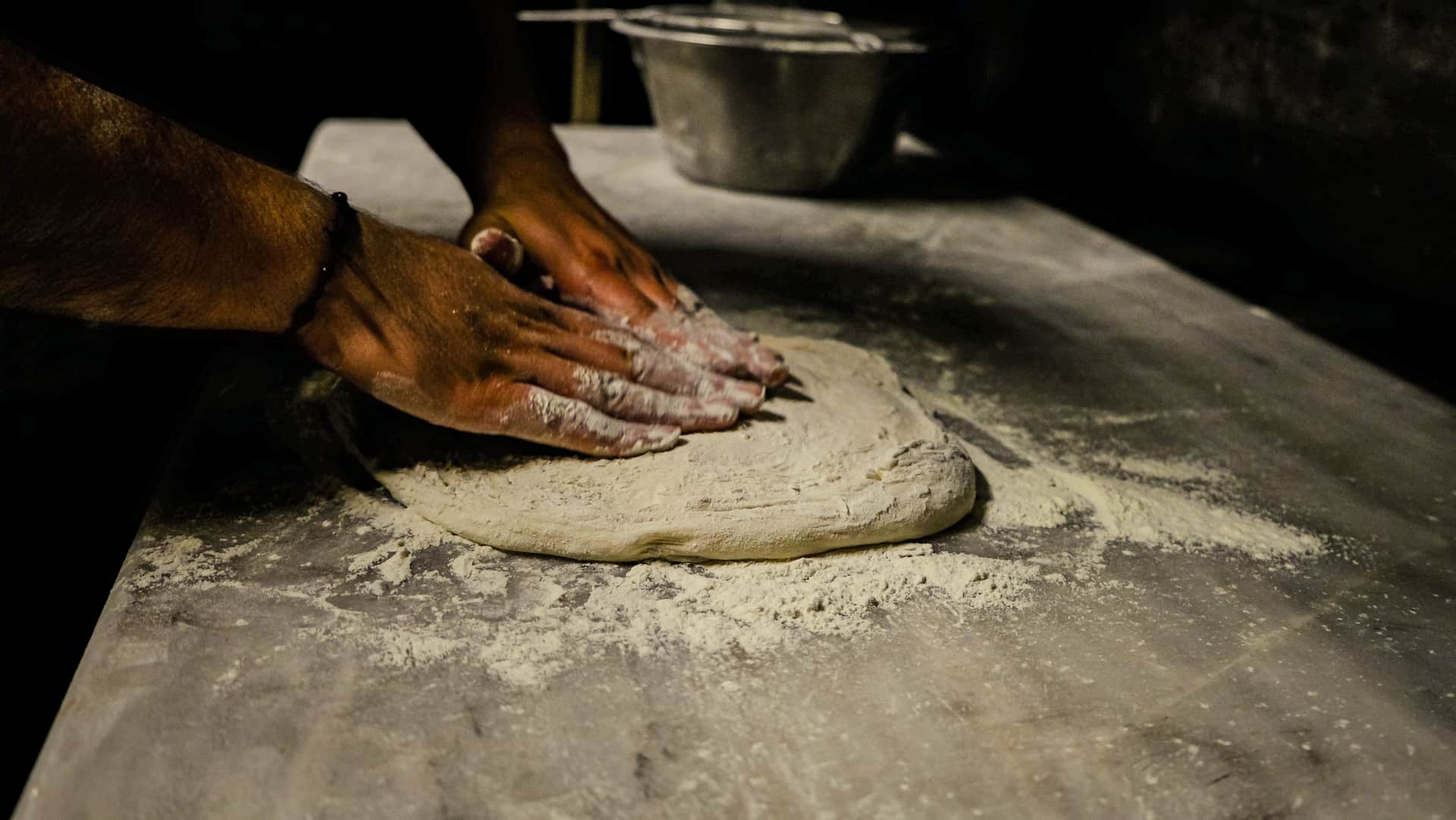 Hands working dough on a floured surface in hard directional light