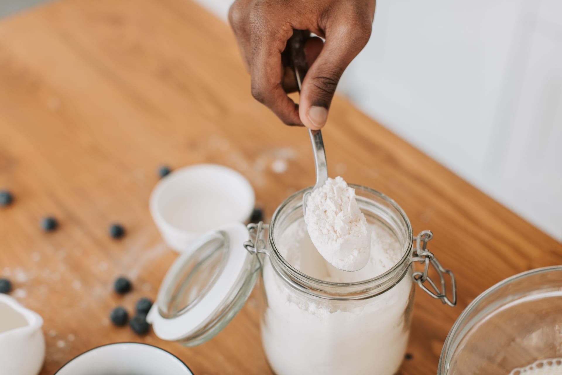 Flour, a wooden spoon and a glass jar on a bare work surface in hard directional light